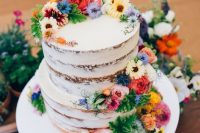 a naked wedding cake with greenery and bright fresh blooms is a lovely idea for a rustic summer wedding