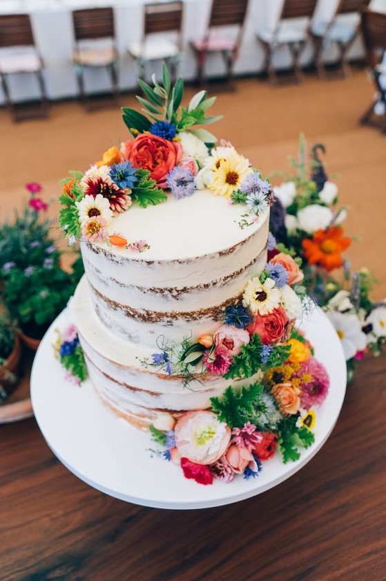 a naked wedding cake with greenery and bright fresh blooms is a lovely idea for a rustic summer wedding