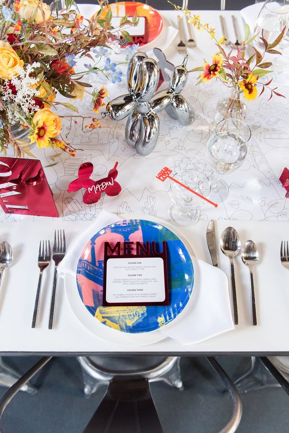 a neutral wedding table setting accented with pop art and Disney inspired stuff, bold blooms and chargers