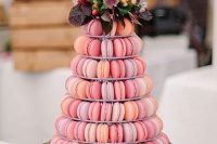a pastel stand with lilac, hot pink and orange macarons, with pastel and bright blooms, greenery and dark foliage is a lovely alternative to a usual wedding cake