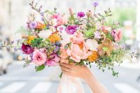 a pretty and bright wedding bouquet of blush, purple, lilac and yellow blooms, greenery and neutral ribbons for summer