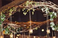 a rustic branch chandelier with greenery and candle holders hanging down is a beautiful and natural decoration