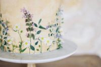 a tan wedding cake with watercolors and pressed edible blooms and leaves is lovely and chic