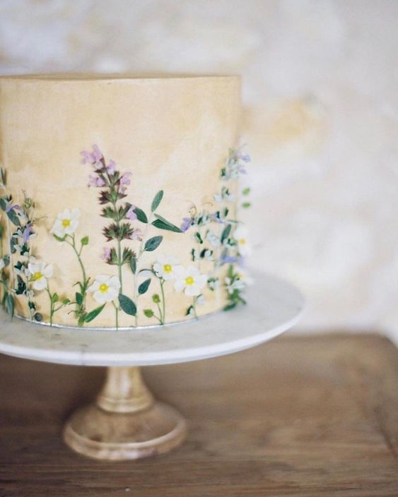 a tan wedding cake with watercolors and pressed edible blooms and leaves is lovely and chic