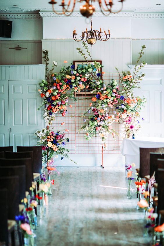 a wedding altar done with super colorful blooms and matching blooms lining up the aisle is gorgeous
