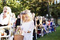 a white lace over the knee dress with long sleeves and a scoop neckline, a flower crown and a basket for a rustic wedding