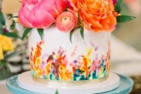 a white wedding cake with bright wateroclor blooms and a gold ribbon plus super bold blooms on top and a calligraphy topper