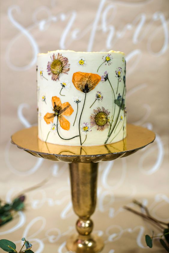 a white wedding cake with pressed edible blooms and leaves is a beautiful summer wedding dessert idea