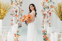 an all-white indoor wedding ceremony space accented with blush, orange and red blooms and white pillar candles
