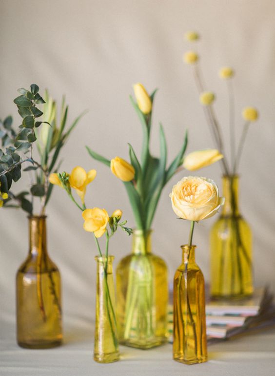 gold, yellow and amber bottles with single blooms in yellow and some greenery form a cluster wedding centerpiece