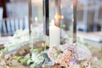 a beach wedding centerpiece with a metal candle lantern, driftwood, peastel blooms and greenery