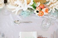 a beach wedding centerpiece with corals, sea sponges, sea glass, driftwood and peachy blooms
