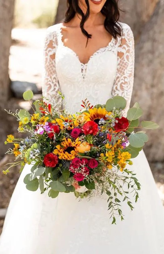 a beautiful colorful wedding bouquet with much textural greenery, red, pink and yellow blooms, sunflowers for a summer or summer to fall wedding