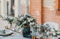 a beautiful pale blue wedding tablescape with a serenity blue tablecloth and vases with white blooms and candles, candles over the table