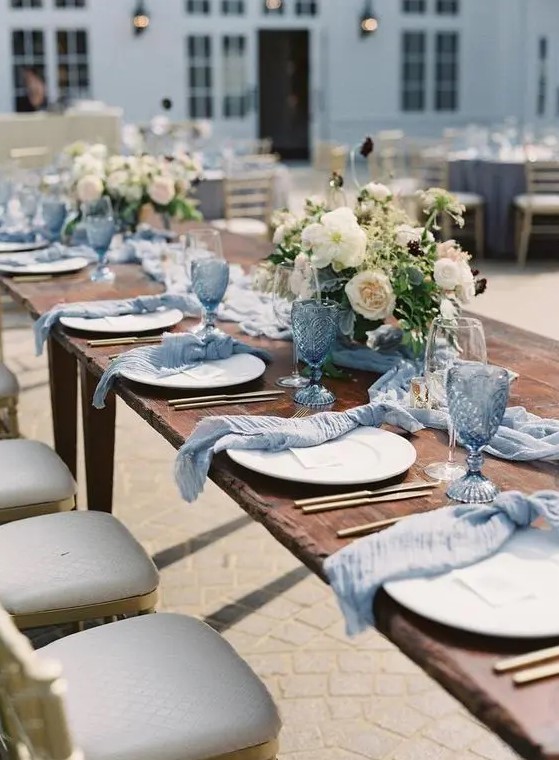 a beautiful wedding tablescape with pale blue glasses and napkins, neutral blooms and greenery and gold cutlery