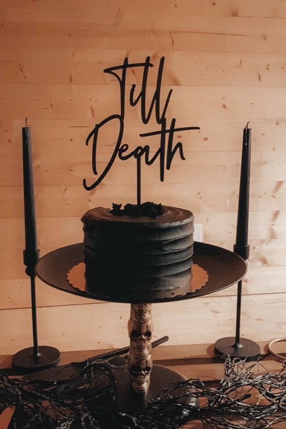 a black buttercream wedding cake topped with some berries and a calligraphy cake topper is a stylish idea for a Halloween wedding