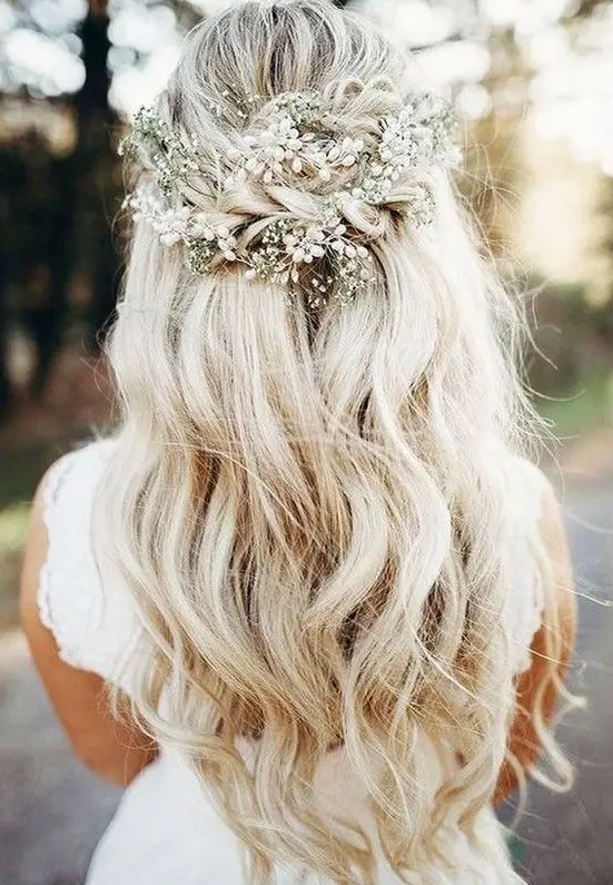 a boho wedding half updo with a volume on top, a braided part and waves down plus a pearl hairpiece and baby's breath
