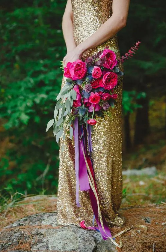a bold jewel-tone wedding bouquet of hot pink blooms, thistles and greenery and long purple and gold ribbons for a bright wedding