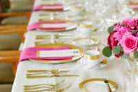 a bold modern wedding tablescape with gold chargers and cutlery and hot pink napkins and blooms is a very stylish and chic idea