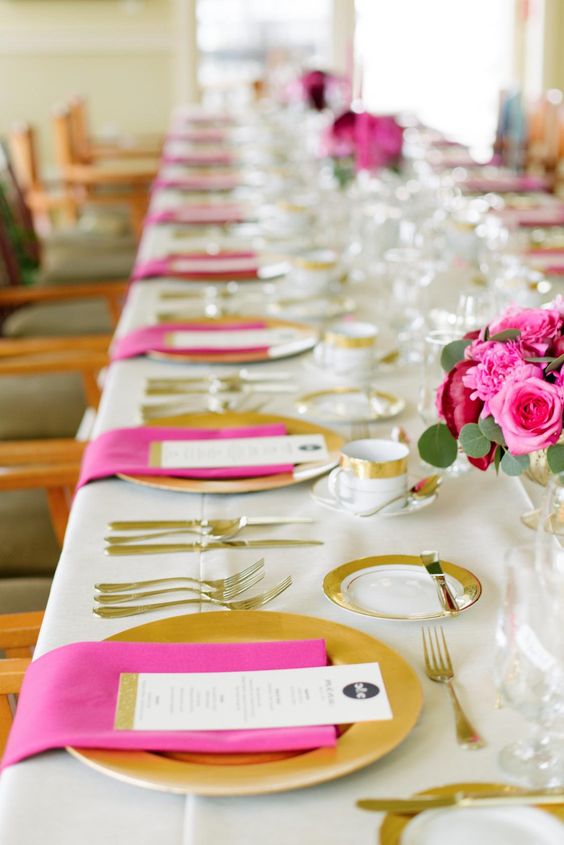 a bold modern wedding tablescape with gold chargers and cutlery and hot pink napkins and blooms is a very stylish and chic idea