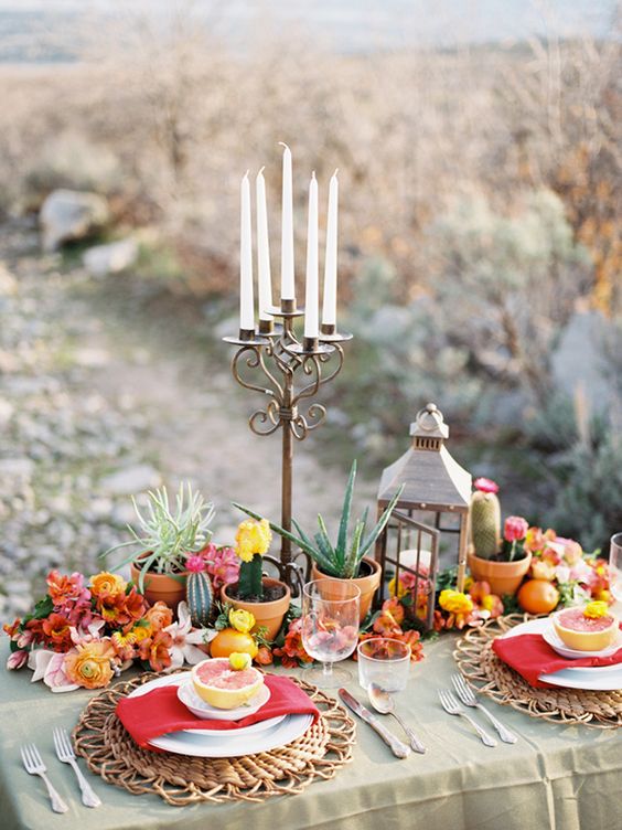 a bold wedding centerpiece of pink, orange and yellow blooms, potted cacti and succulents plus candles