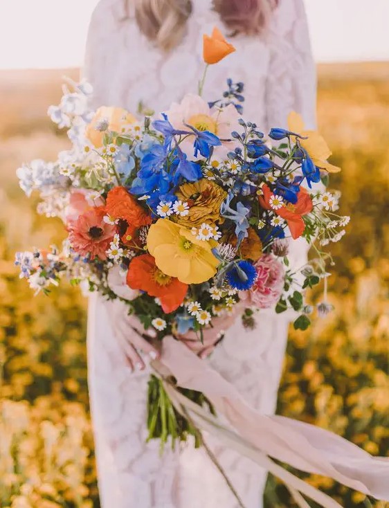 a bold wildflower bouquet in the shades of blue, orange, yellow and with blush ribbons