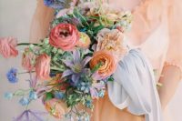 a bright and chic wedding bouquet of pink and orange ranunculus, blue and purple blooms, greenery and blue ribbons