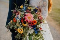 a bright cascading wedding bouquet with pink, orange, yellow and blue blooms and greenery is amazing for summer