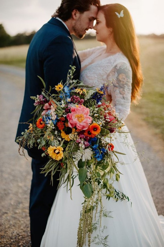 a bright cascading wedding bouquet with pink, orange, yellow and blue blooms and greenery is amazing for summer