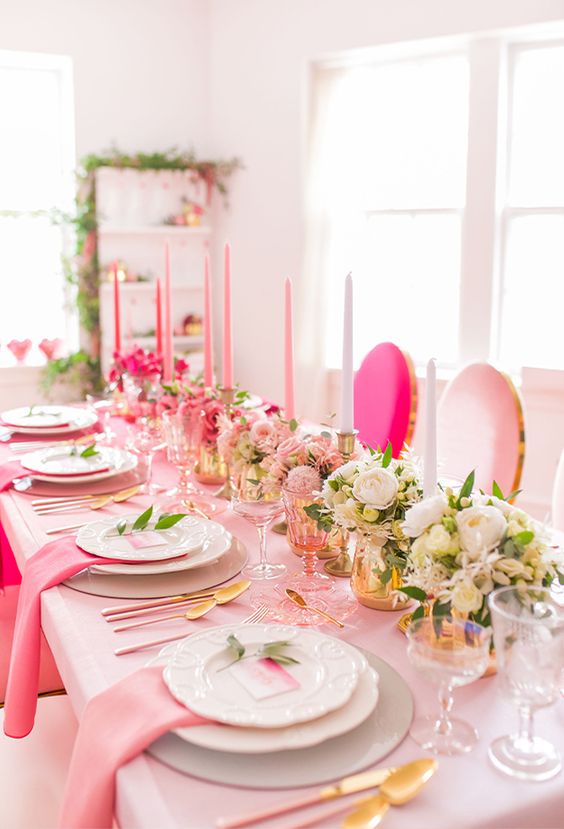 a bright pink wedding tablescape with pink linens, ombre pink candles, white and pink blooms and gold cutlery