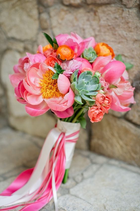 a bright wedding bouquet of pink peonies, orange ranunculus, succulents and pink and neutral ribbon is a lovely solution for summer