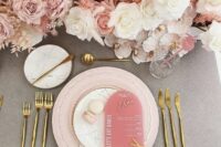 a chic modern wedding tablescape with light pink and white florals, light pink plates and a pink menu, gold cutlery