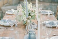 a chic pale blue wedding tablescape with pale blue linens, candles and candleholders, blush blooms and greenery