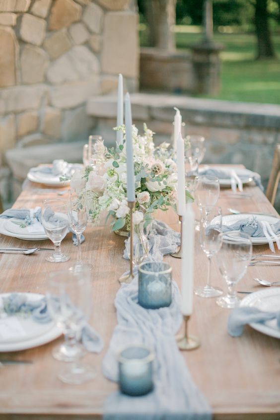 a chic pale blue wedding tablescape with pale blue linens, candles and candleholders, blush blooms and greenery