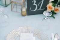 a chic wedding table setting with a pale blue tablecloth, a gilded plate, peachy blooms and neutral napkins