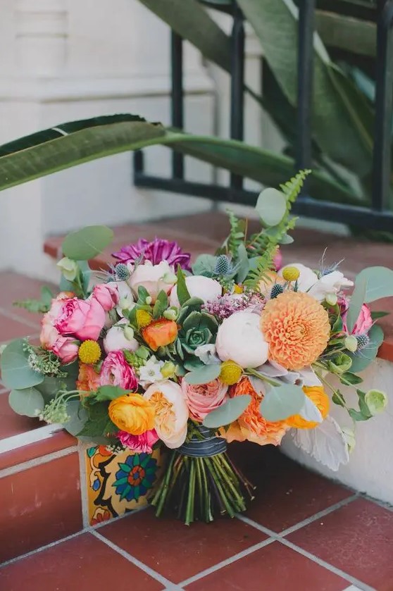 a colorful bouquet with purple, pink, orange and blush blooms and lots of ferns and eucalyptus