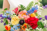 a colorful wedding bouquet of yellow, orange, hot red, pink, blue and purple blooms and greenery plus long matching ribbons
