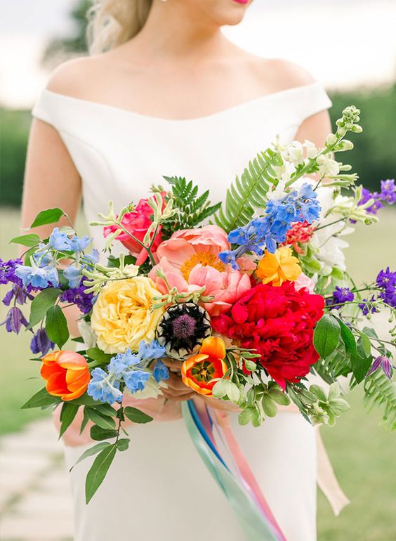 a colorful wedding bouquet of yellow, orange, hot red, pink, blue and purple blooms and greenery plus long matching ribbons