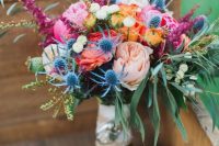 a colorful wedding bouquet with blush, pink, orange and yellow blooms, greenery and thistles is pretty and fun