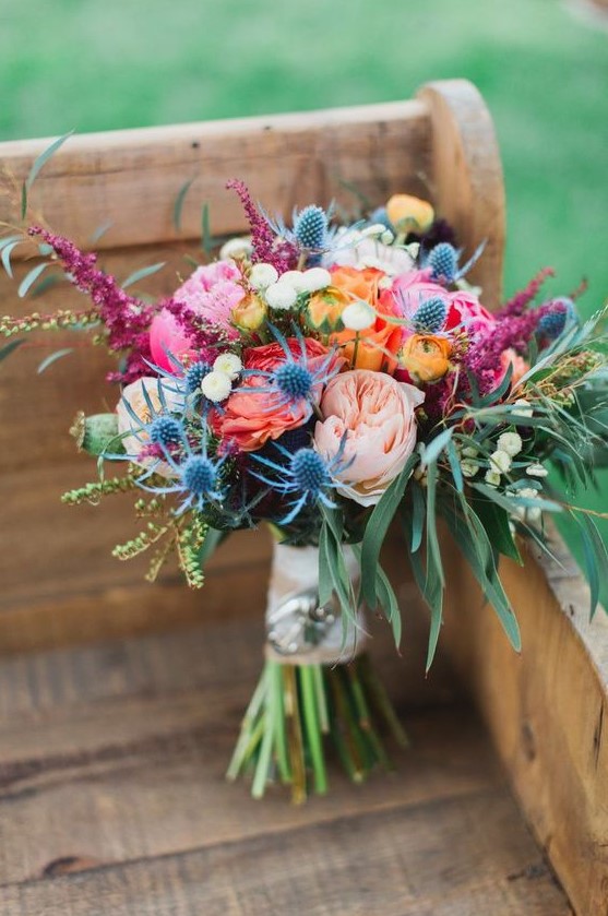 a colorful wedding bouquet with blush, pink, orange and yellow blooms, greenery and thistles is pretty and fun
