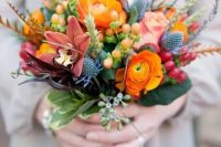 a colorful wedding bouquet with orange ranunculus, thistles, dark lilies, berries and grasses for a color-loving bride