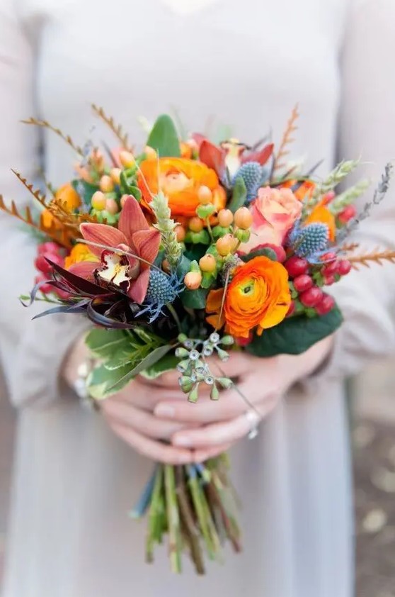a colorful wedding bouquet with orange ranunculus, thistles, dark lilies, berries and grasses for a color loving bride