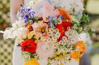 a colorful wedding bouquet with pink and yellow ranunculus, white and blush blooms, bold red touches and greenery