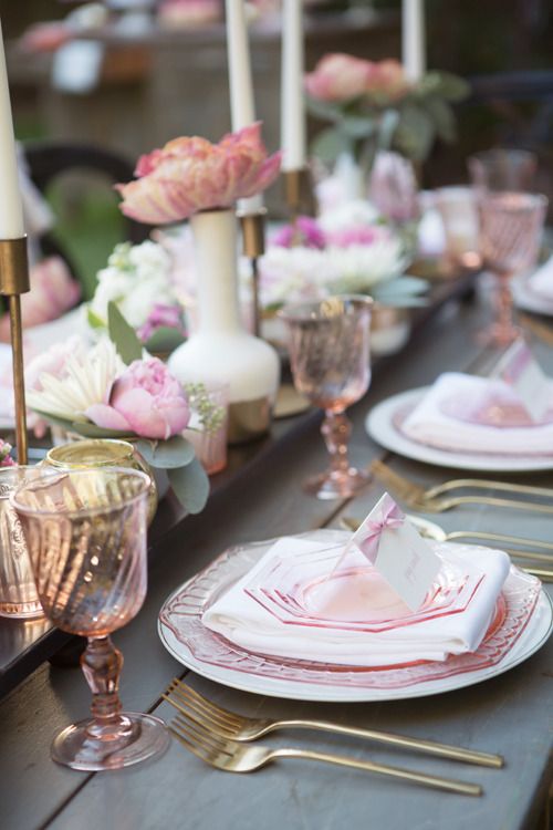 a cool and casual wedding tablescape with pink blooms and plates, pink glasses and gold cutlery, gold candleholders