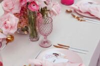 a cool pink wedding tablescape with blush plates and napkins, light and hot pink blooms, pink glasses and hot pink candleholders