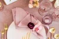 a cool wedding tablescape with pink blooms, a pale pink tablecloth and napkin, pale pink and mauve glasses and gold cutlery