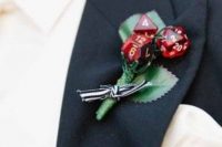 a creative wedding boutonniere of silk leaves, red dices and a striped bow is a fun idea for a groom who loves to play