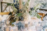 a delicate and elegant wedding tablescape with pale blue chargers and glasses, a watercolor table number, white and blue bloom centerpiece