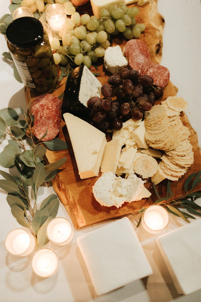 a deliciously styled charcuterie board with various cheese, salami, grapes and decorated with candles and greenery