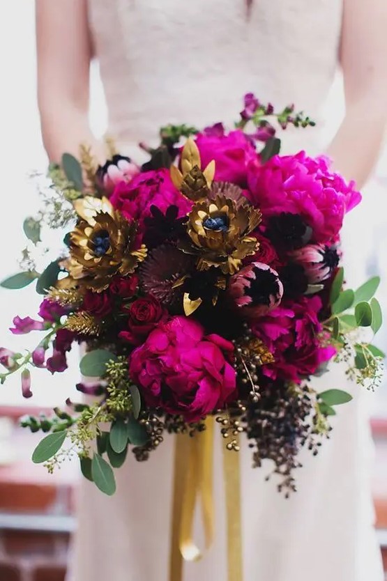 a dramatic bridal bouquet of hot pink peonies, deep purple blooms, gold faux flowers, greenery and gilded seeded eucalyptus